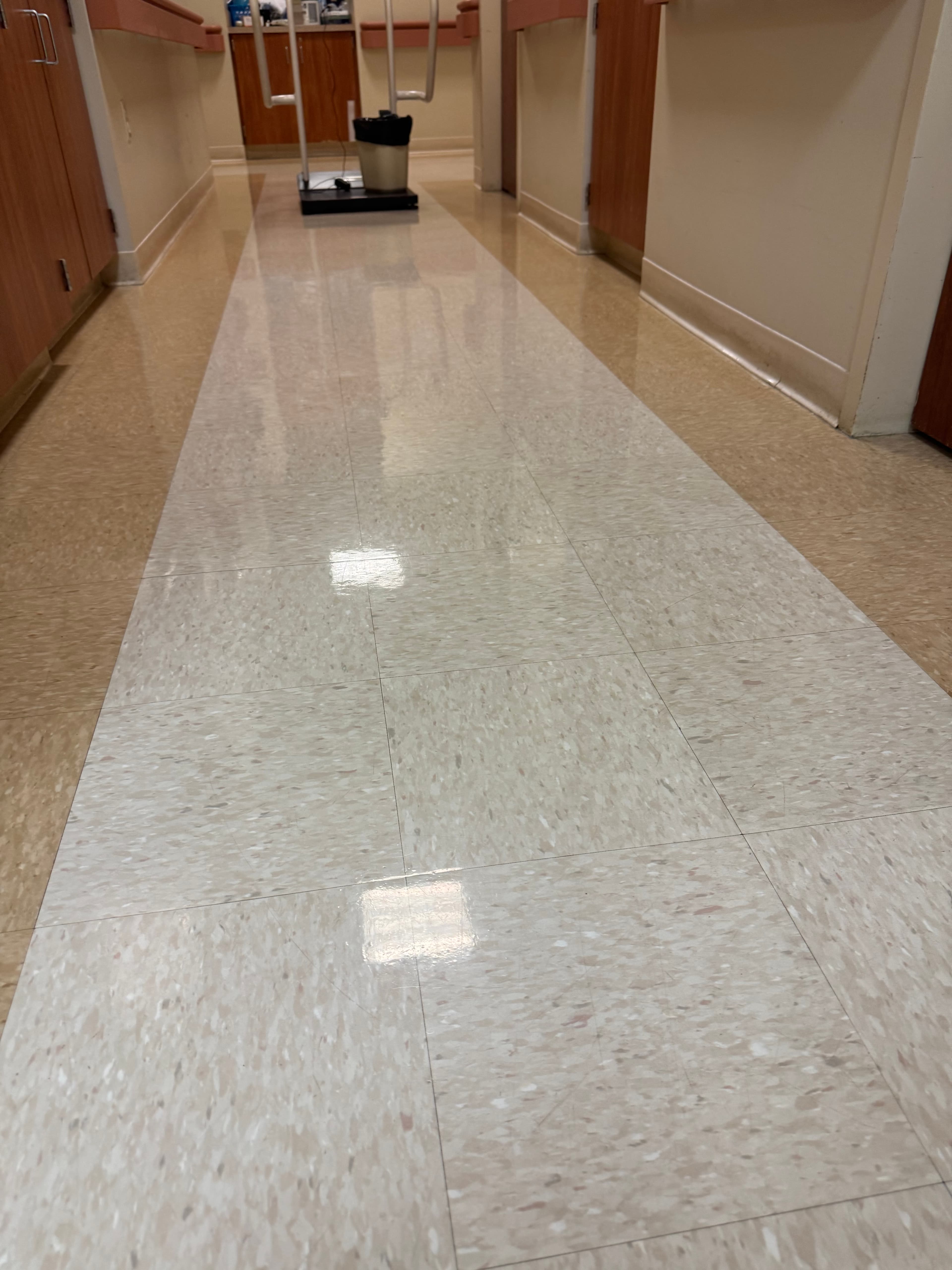 Polished tile floor in a bright hospital corridor with wooden cabinets and medical equipment.